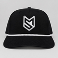Load image into Gallery viewer, A black trucker-style cap with a white embroidered geometric logo on the front, displayed on a white chair in front of white paneled doors.
