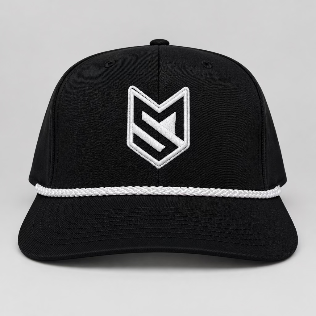 A black trucker-style cap with a white embroidered geometric logo on the front, displayed on a white chair in front of white paneled doors.