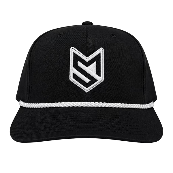 A black trucker-style cap with a white embroidered geometric logo on the front, displayed on a white chair in front of white paneled doors.