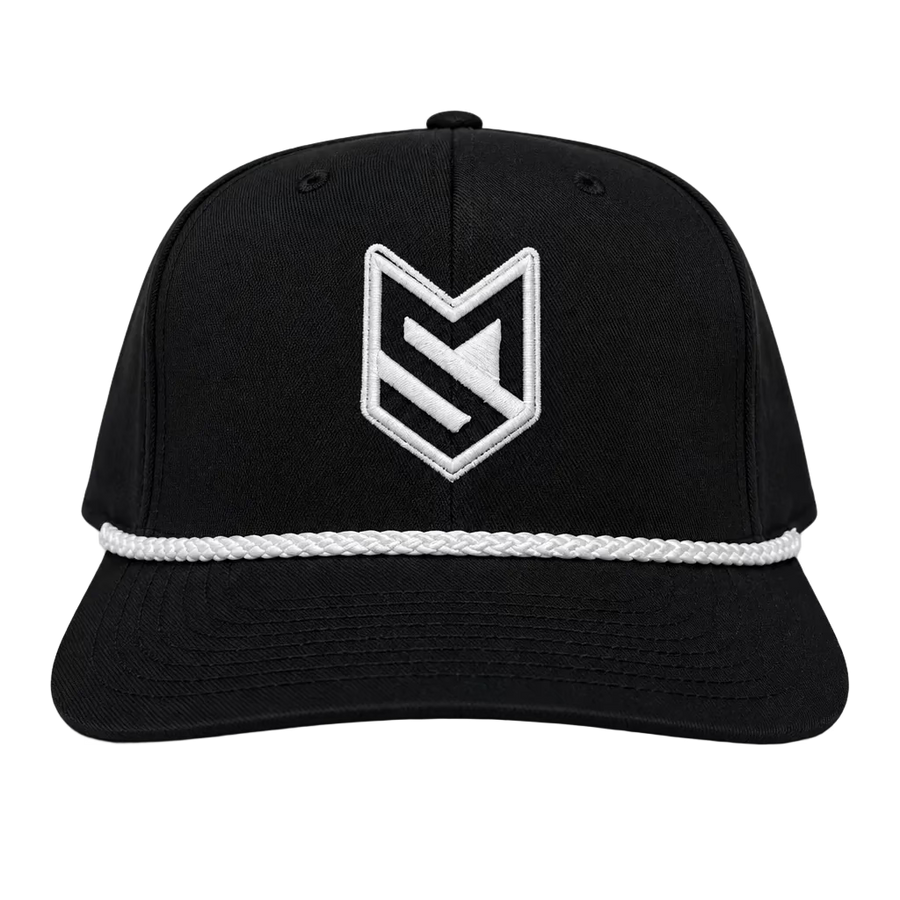 A black trucker-style cap with a white embroidered geometric logo on the front, displayed on a white chair in front of white paneled doors.